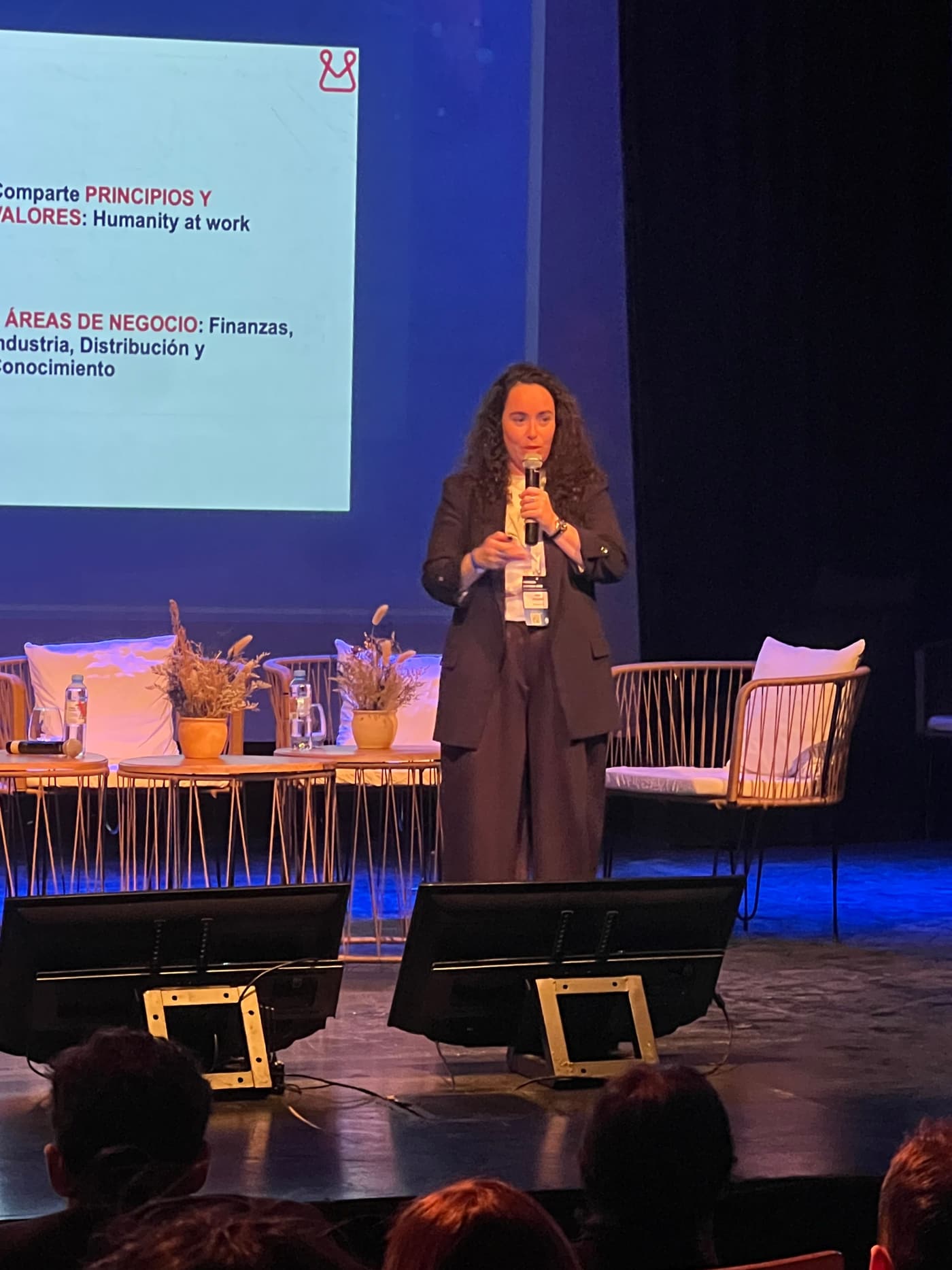 Speaker holding a microphone on stage, next to a screen showing the Mondragón presentation